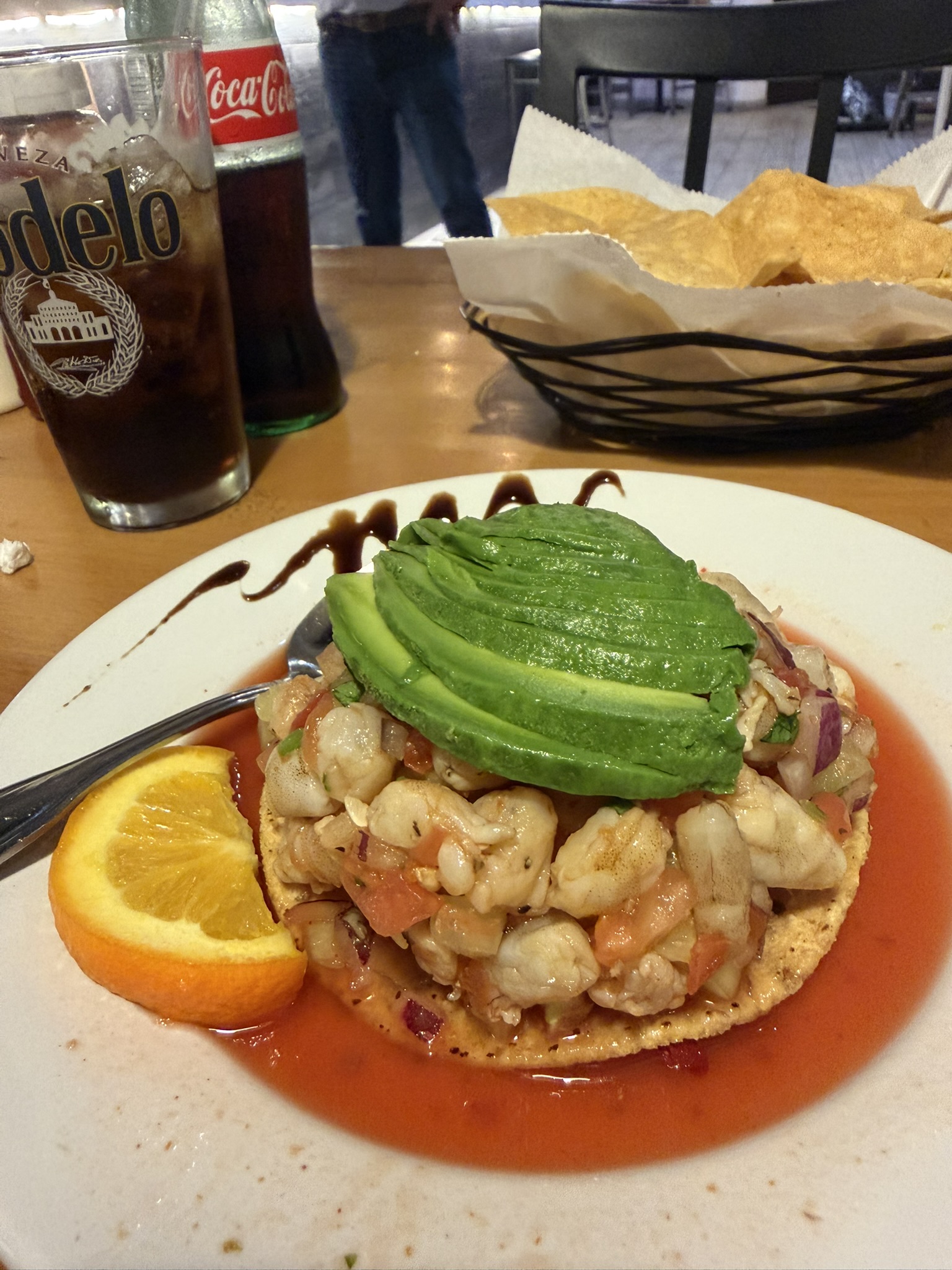 Shrimp ceviche tostada with avocado fan, reddish marinade, and orange wedge garnish